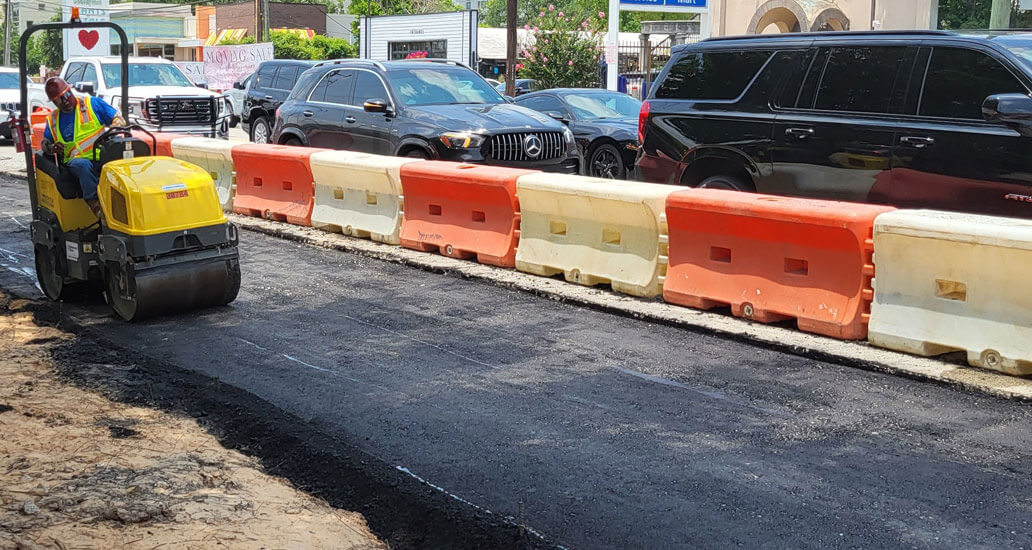 Construction worker drives steel roller flatting the black asphalt surface on the corner of Westheimer and Weslayne.